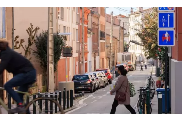 Rue avec présence d'une piétonne et d'un cycliste accompagnés de panneaux indiquant la présence d'une vélorue