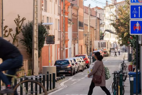 Rue avec présence d'une piétonne et d'un cycliste accompagnés de panneaux indiquant la présence d'une vélorue