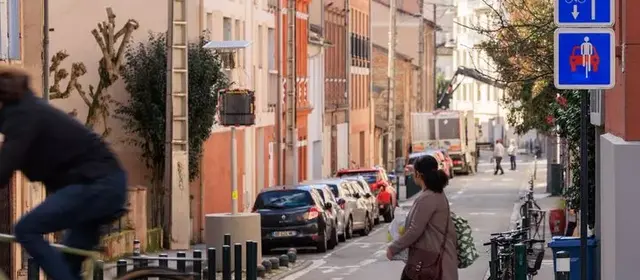 Rue avec présence d'une piétonne et d'un cycliste accompagnés de panneaux indiquant la présence d'une vélorue